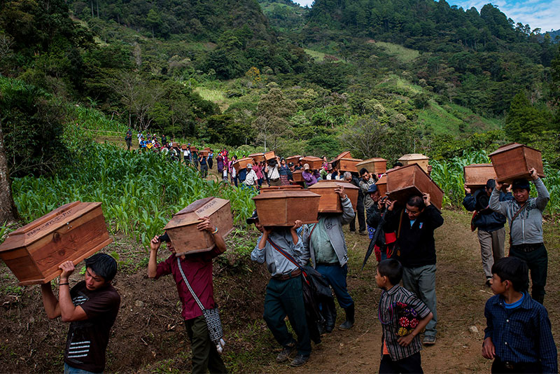 Indigenous villagers carry coffins down a mountain path during a burial ceremony for victims of past Guatemalan violence.