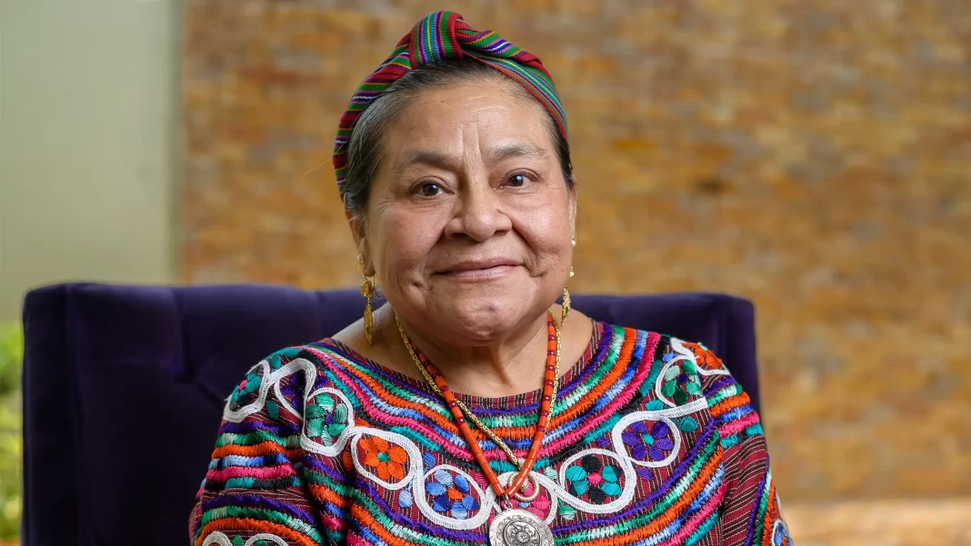 A photo of Rigoberta Menchú smiling at the camera in traditional Mayan dress.