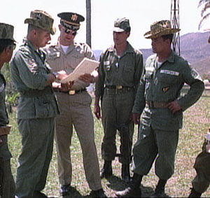 Two U.S. military officials stand with a soldier, a Colonel, and a Sergeant of the Guatemalan Army, reading a document.